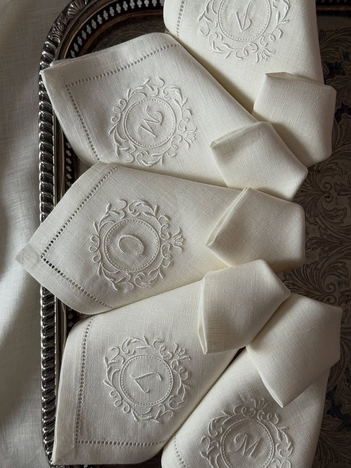 White linen napkins with embroidered monograms arranged on a silver decorative tray.