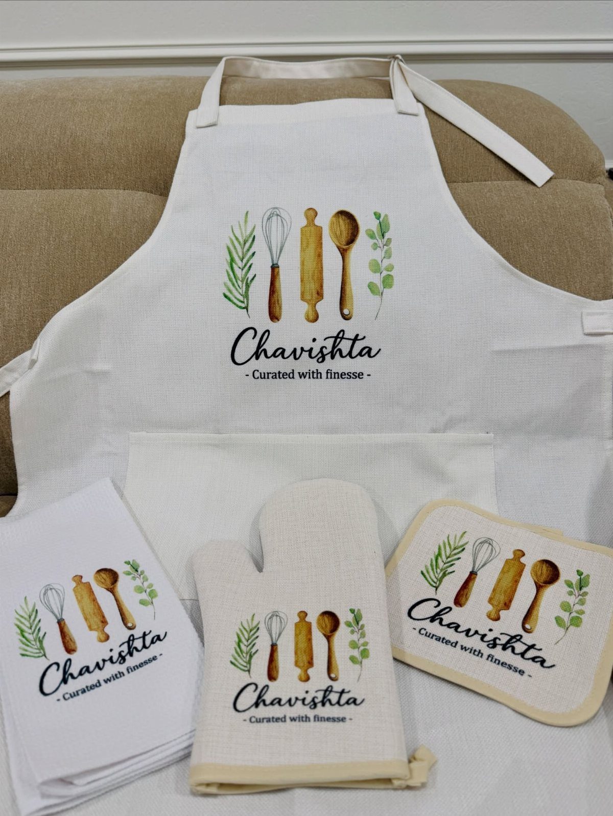 White personalized apron and matching kitchen linens with utensil illustrations and name.