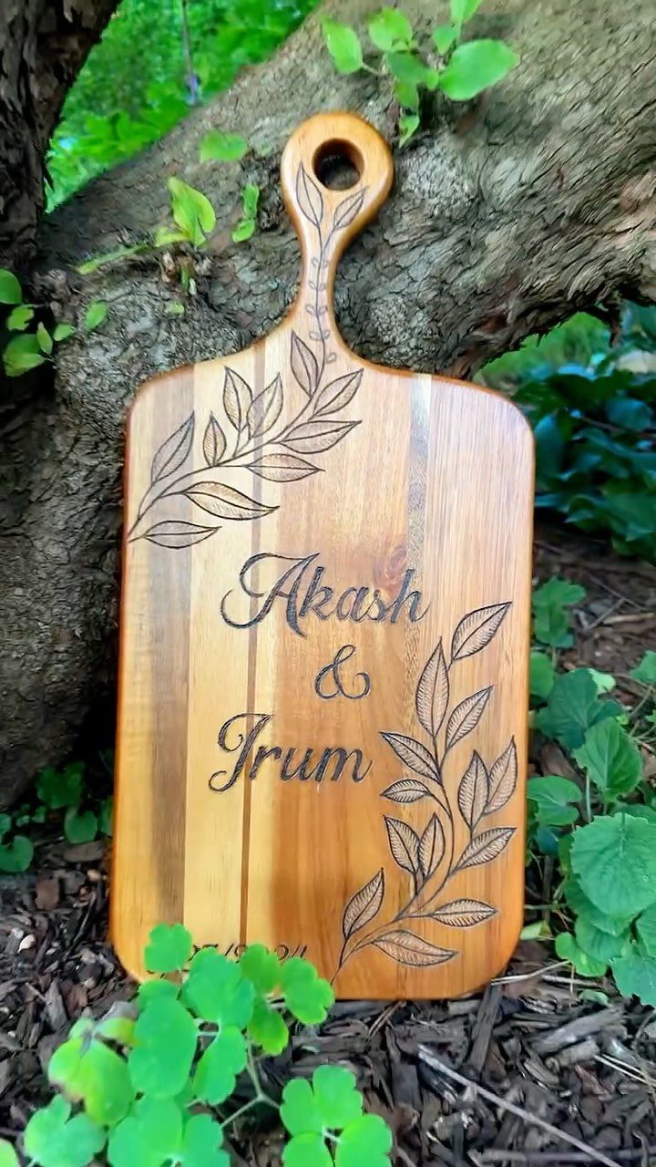 Wooden cutting board engraved with names and leaves leaning against a tree trunk.