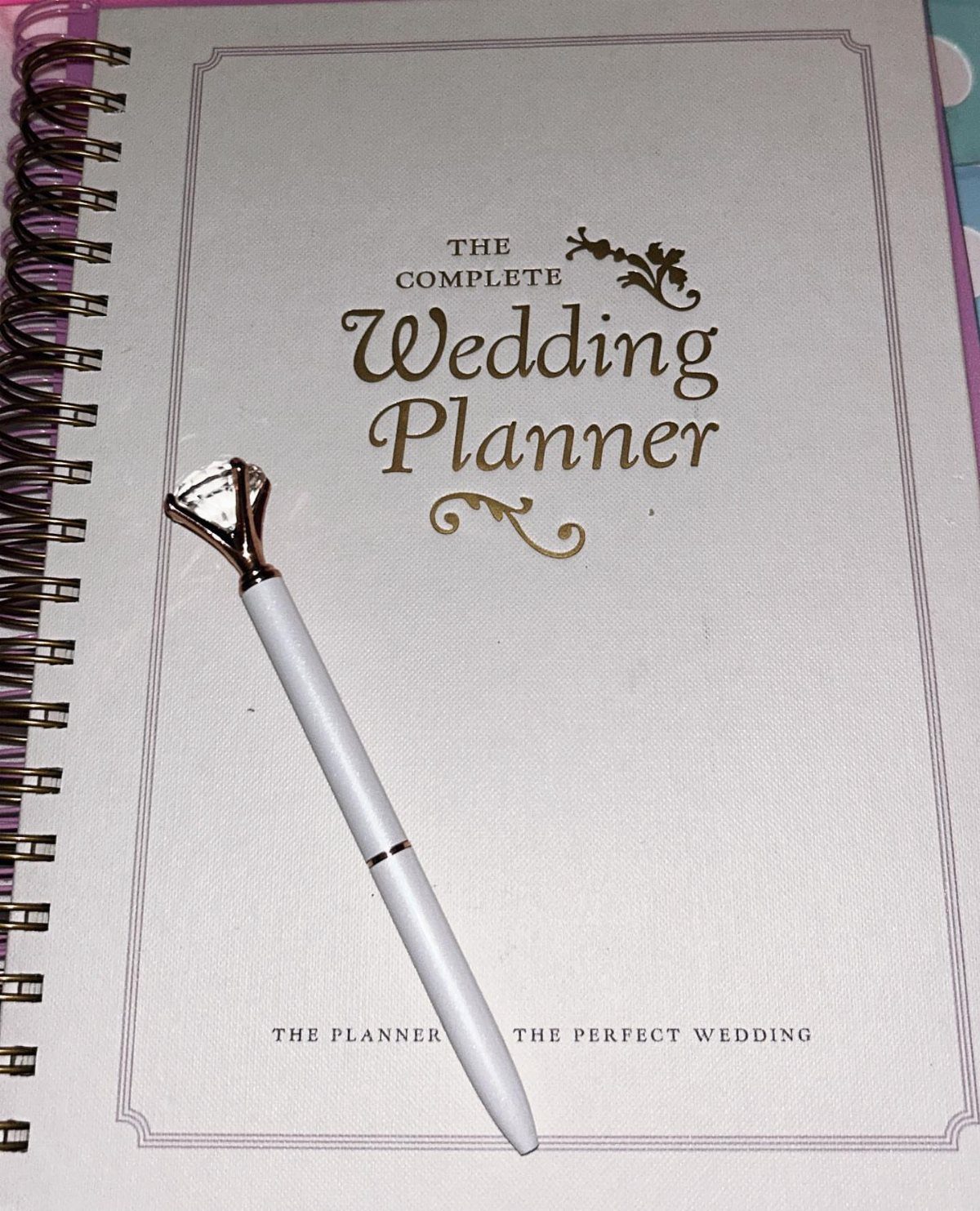 Wedding planner notebook with a diamond-topped white pen resting on the cover.