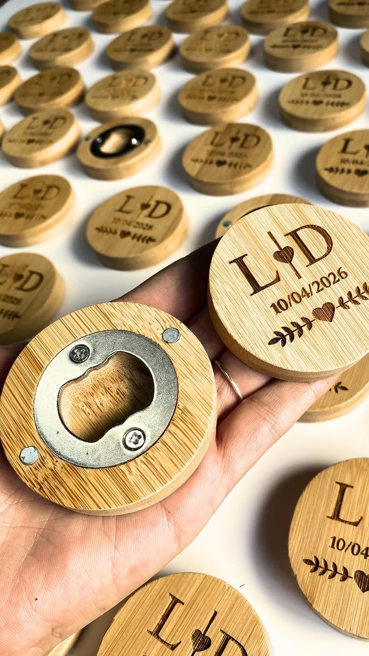 Circular wooden bottle openers with engraved wedding initials and date held in hand.