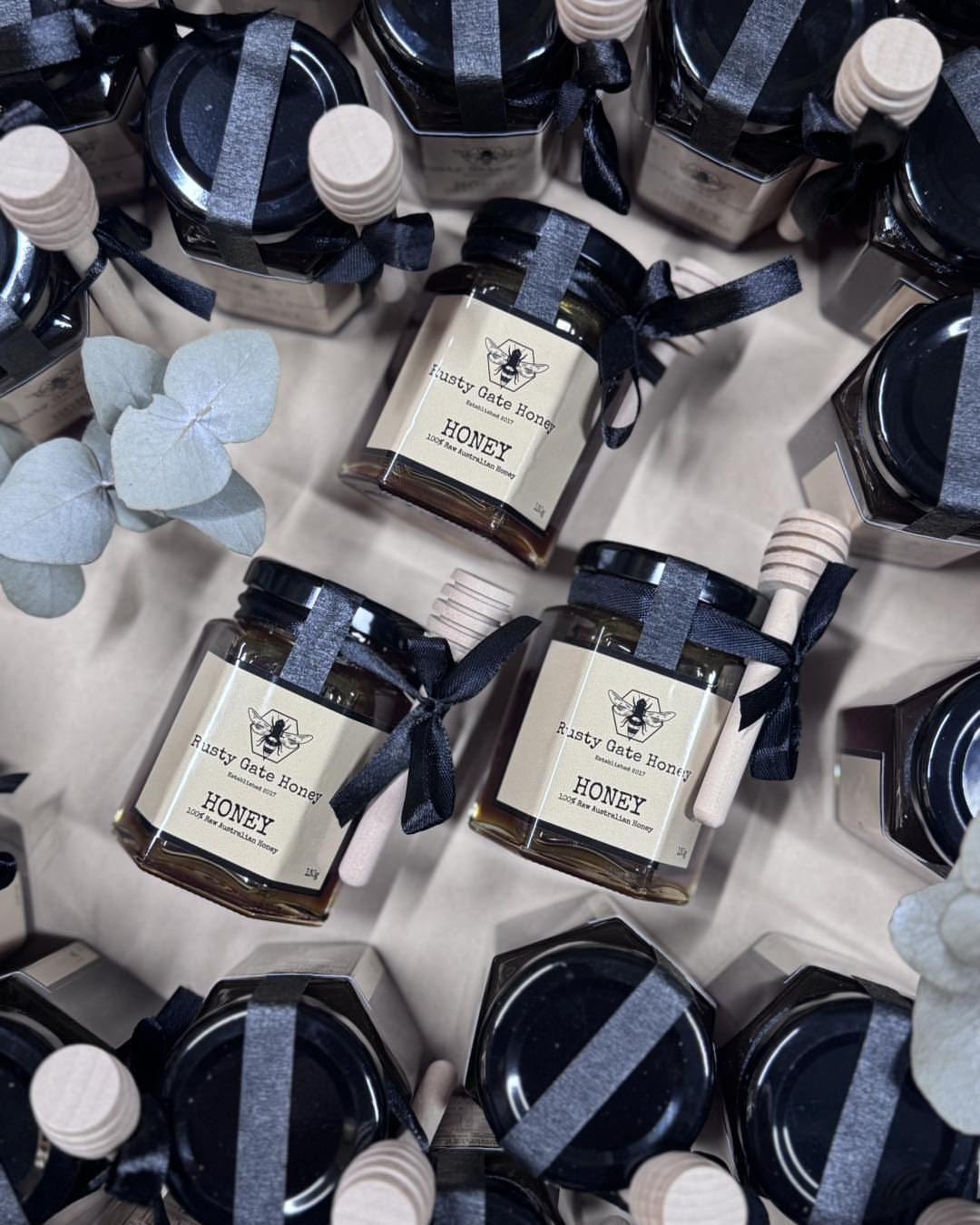 Small honey jars with wooden dippers and blue ribbons as wedding favors.