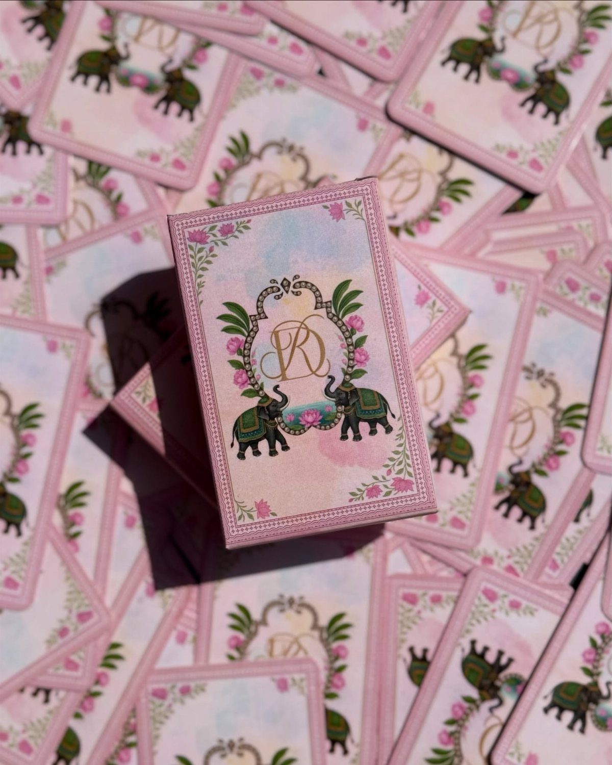 Custom pink playing cards with green elephants and a monogram scattered on a table.