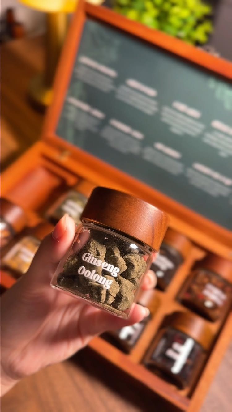 Small glass jar of Ginseng Oolong tea held over a wooden gift set.