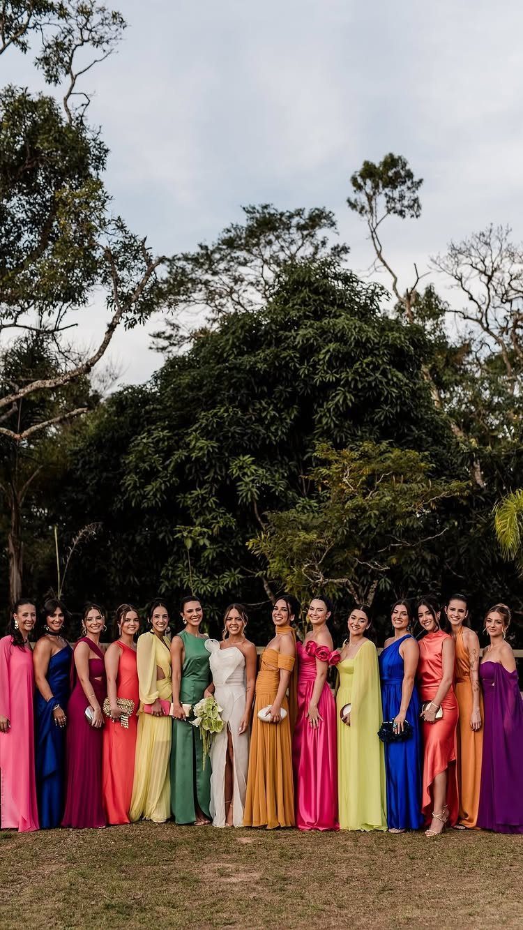 Women in a variety of colorful long bridesmaids dresses standing in a grassy field.