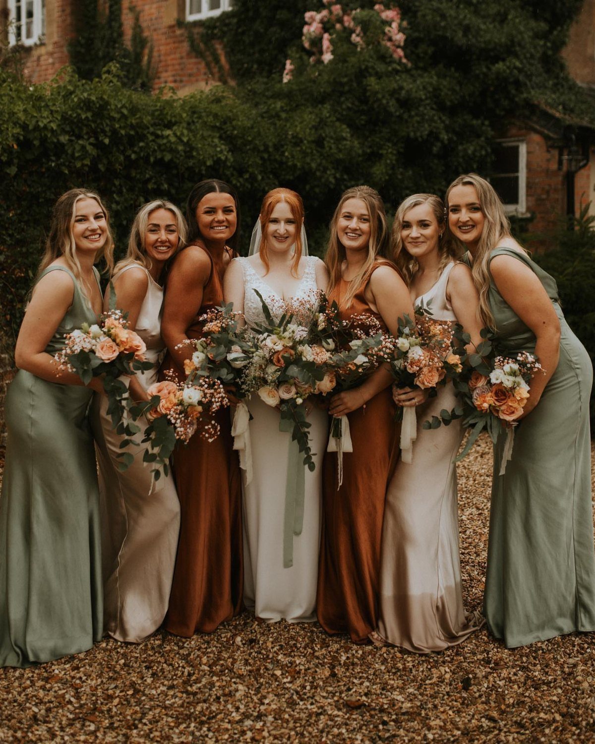 Bride and bridesmaids posing in mismatched sage, champagne, and rust colored dresses.