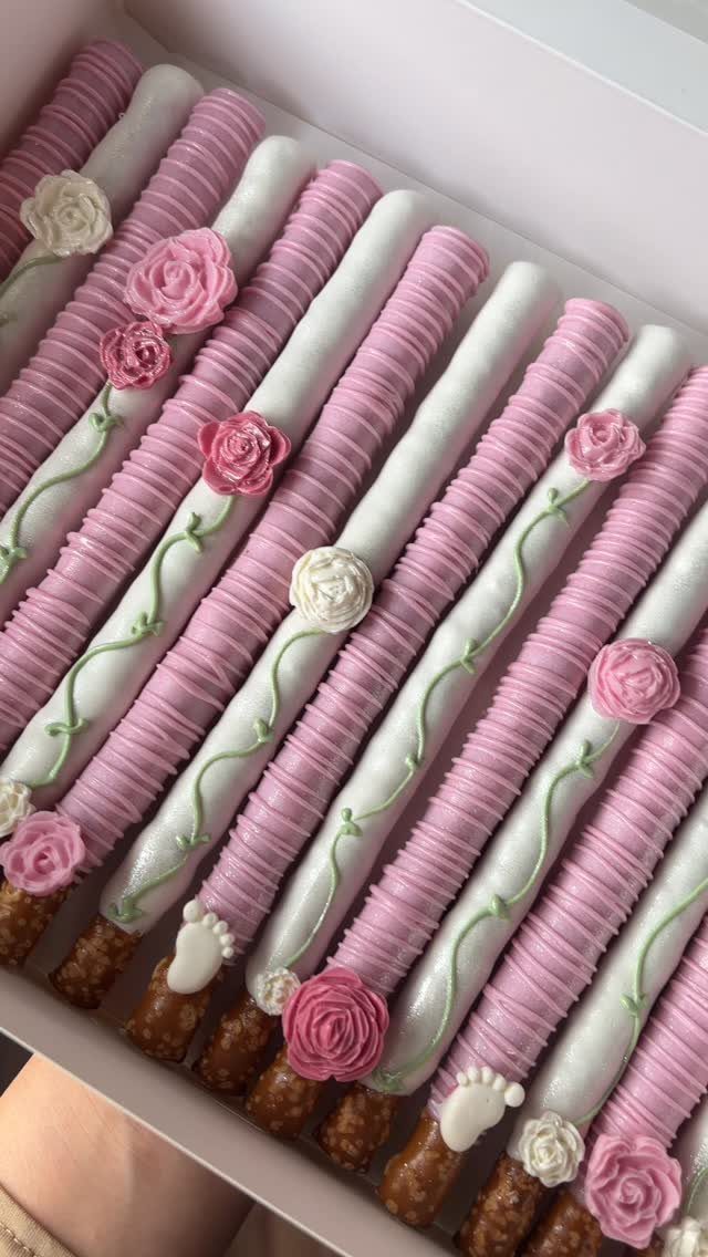 Chocolate-dipped pretzel rods decorated with pink and white frosting and small roses.