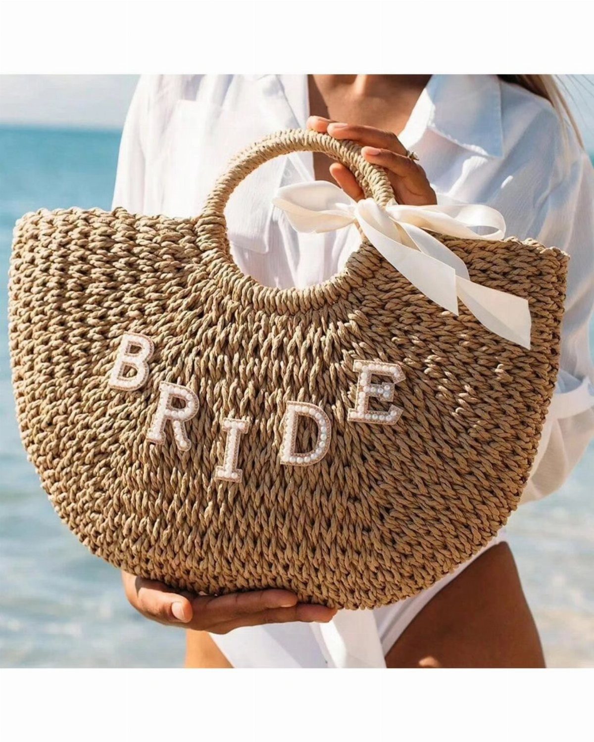 Woven straw tote bag with pearl BRIDE lettering and white ribbon bow.