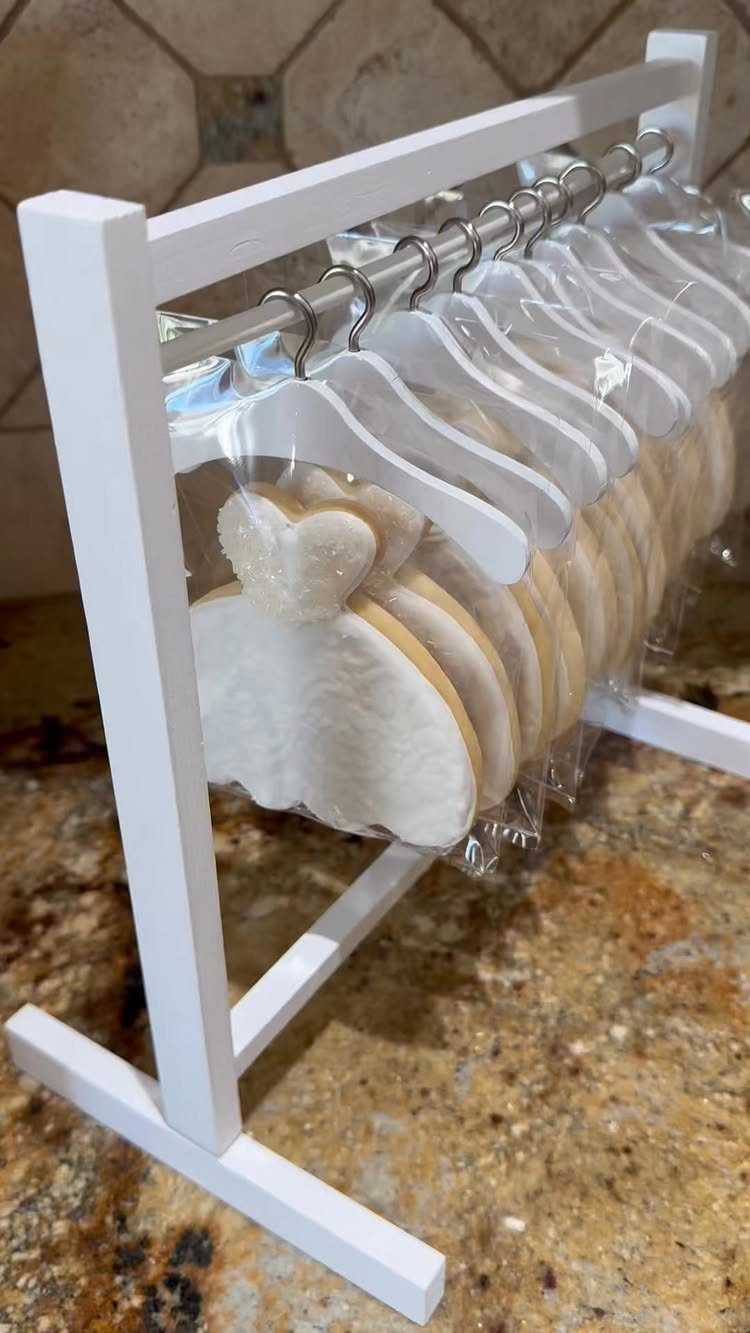 Wedding dress shaped cookies on tiny white hangers displayed on a wooden rack