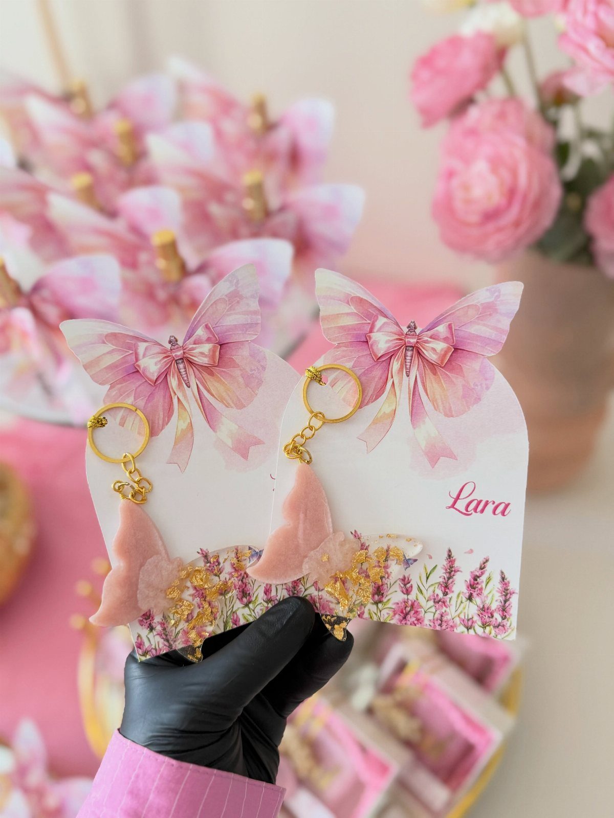 Butterfly keychains on white cards with floral designs held by a gloved hand.