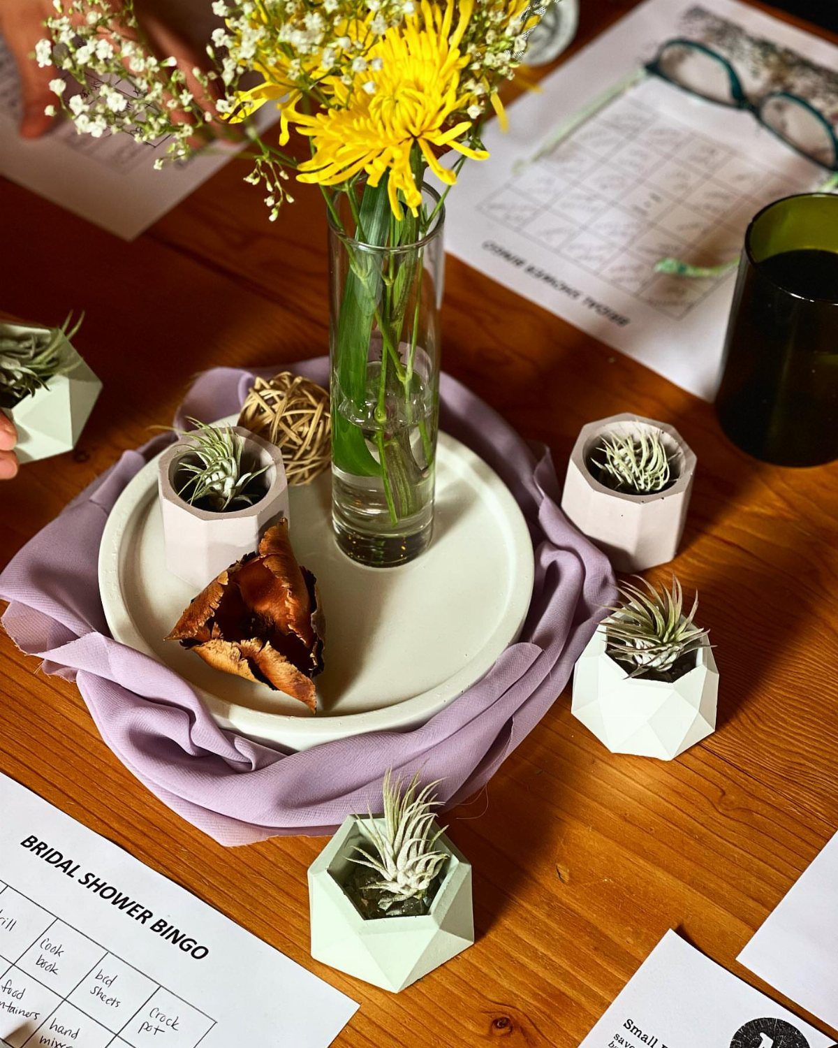 Air plants in geometric concrete pots on a wooden table with yellow flowers.