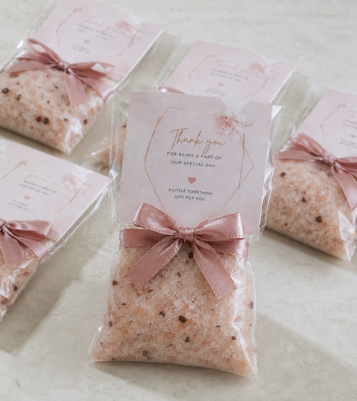 Pink bath salts in clear bags with rose ribbons and thank you cards.