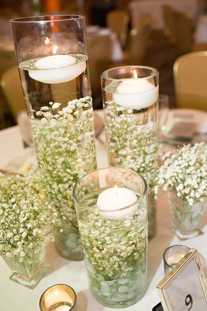 Glass cylinder vases with baby's breath and floating white candles on a table.