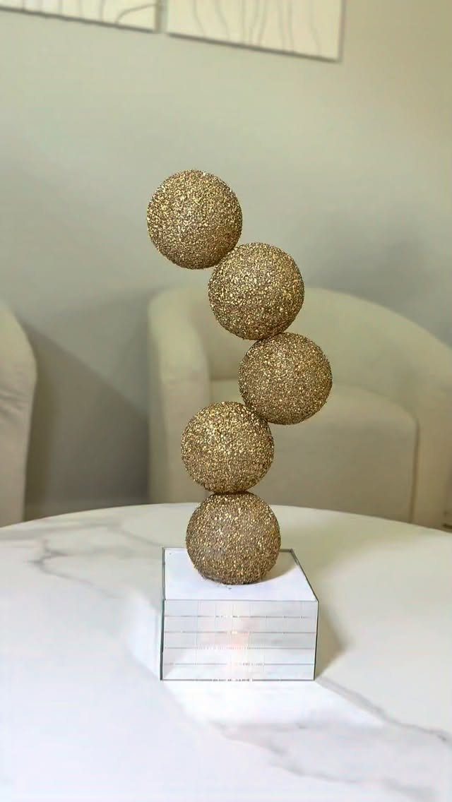 Gold glitter spheres stacked on a square mirrored base on a marble table.