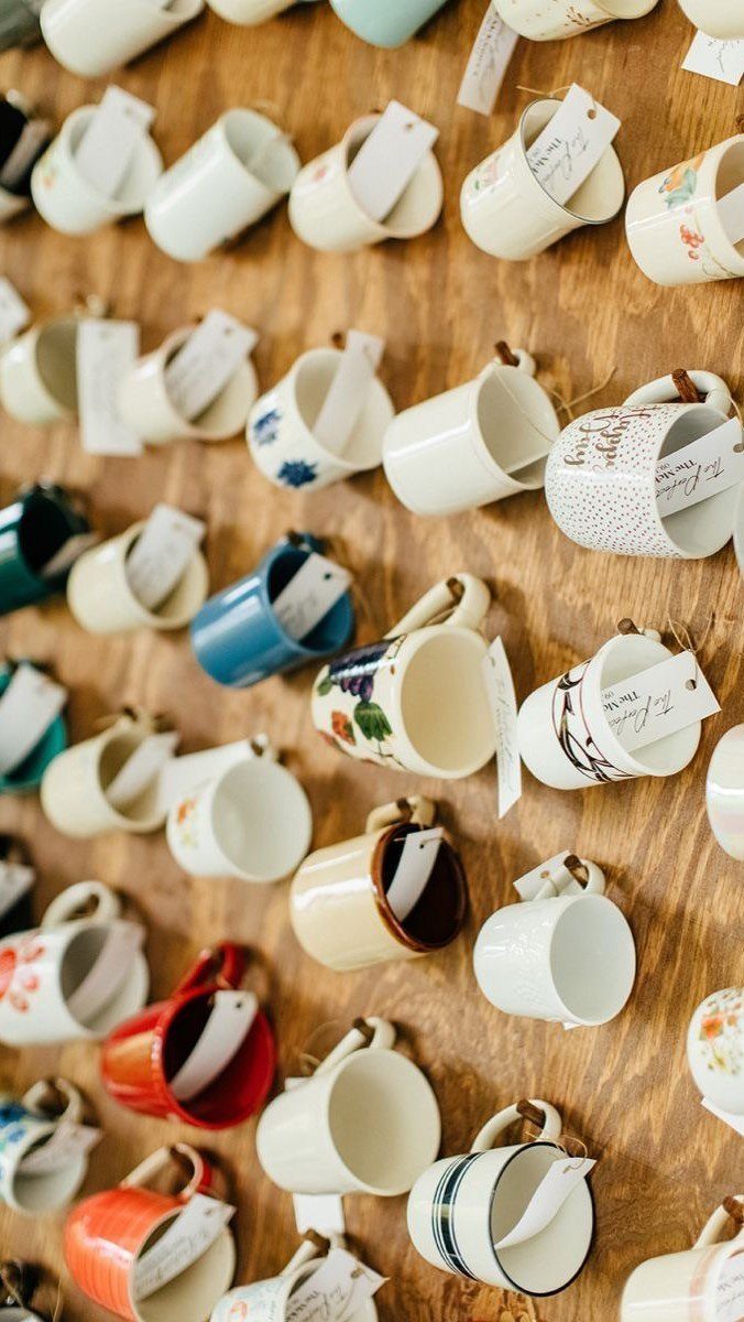 Ceramic mugs with tags hanging on a rustic wooden wall in a grid.