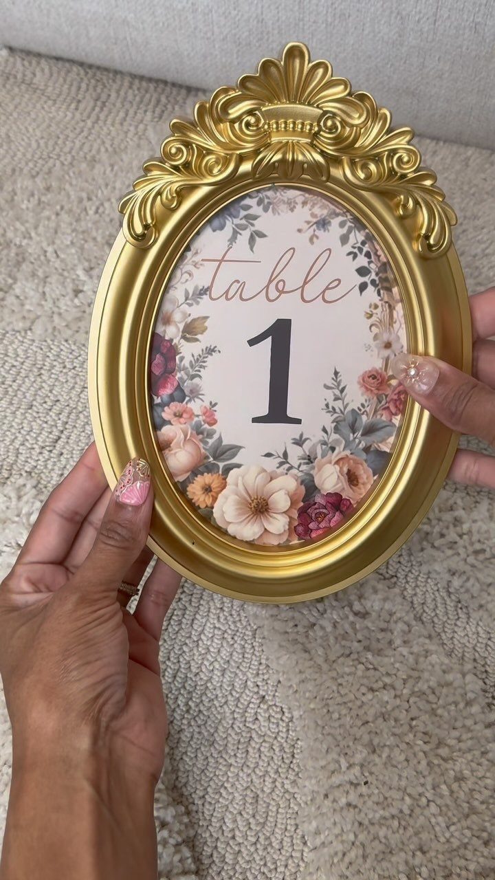 Ornate gold oval frame displaying a floral table number one for a wedding.