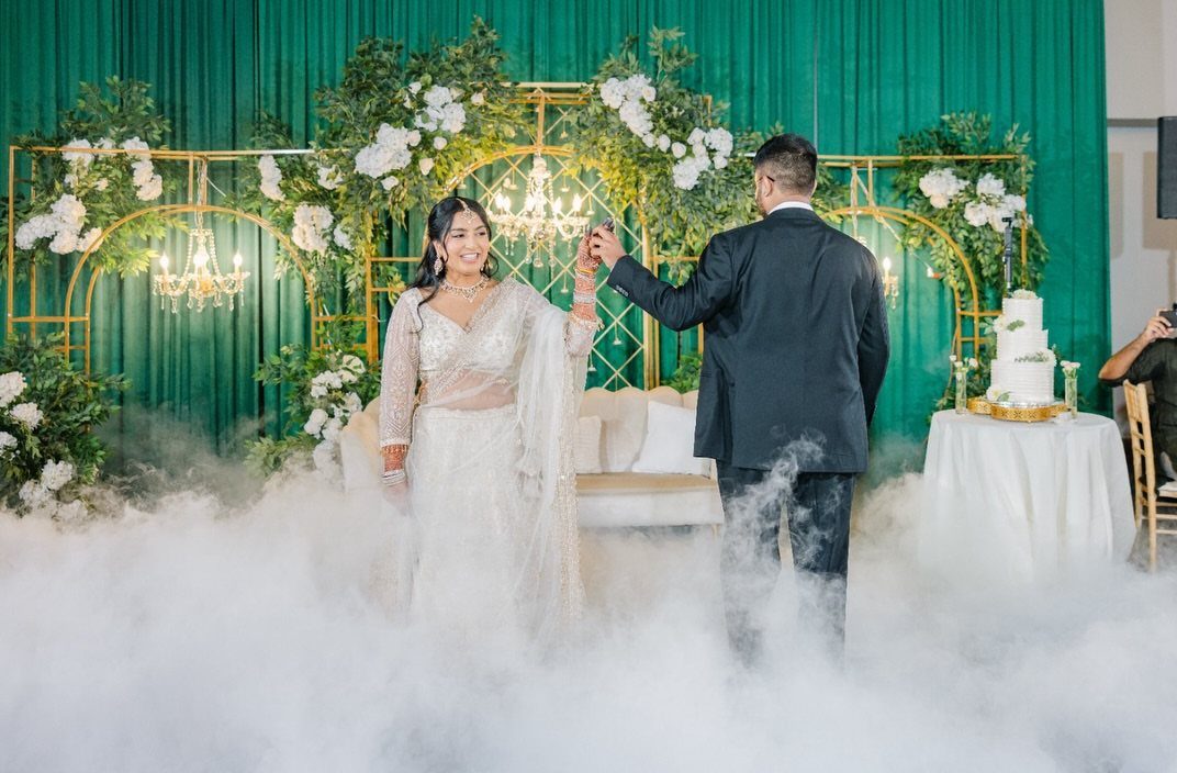 Couple dancing in fog before emerald green curtains and a gold floral arch.
