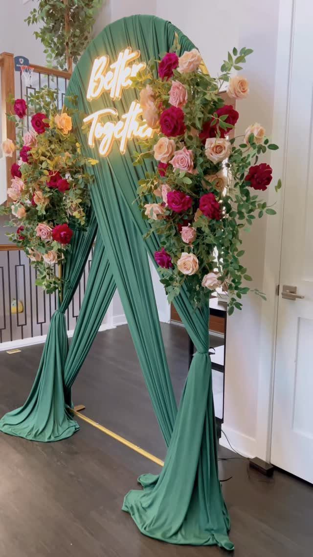 Emerald green draped wedding arch with red and pink roses and neon sign.