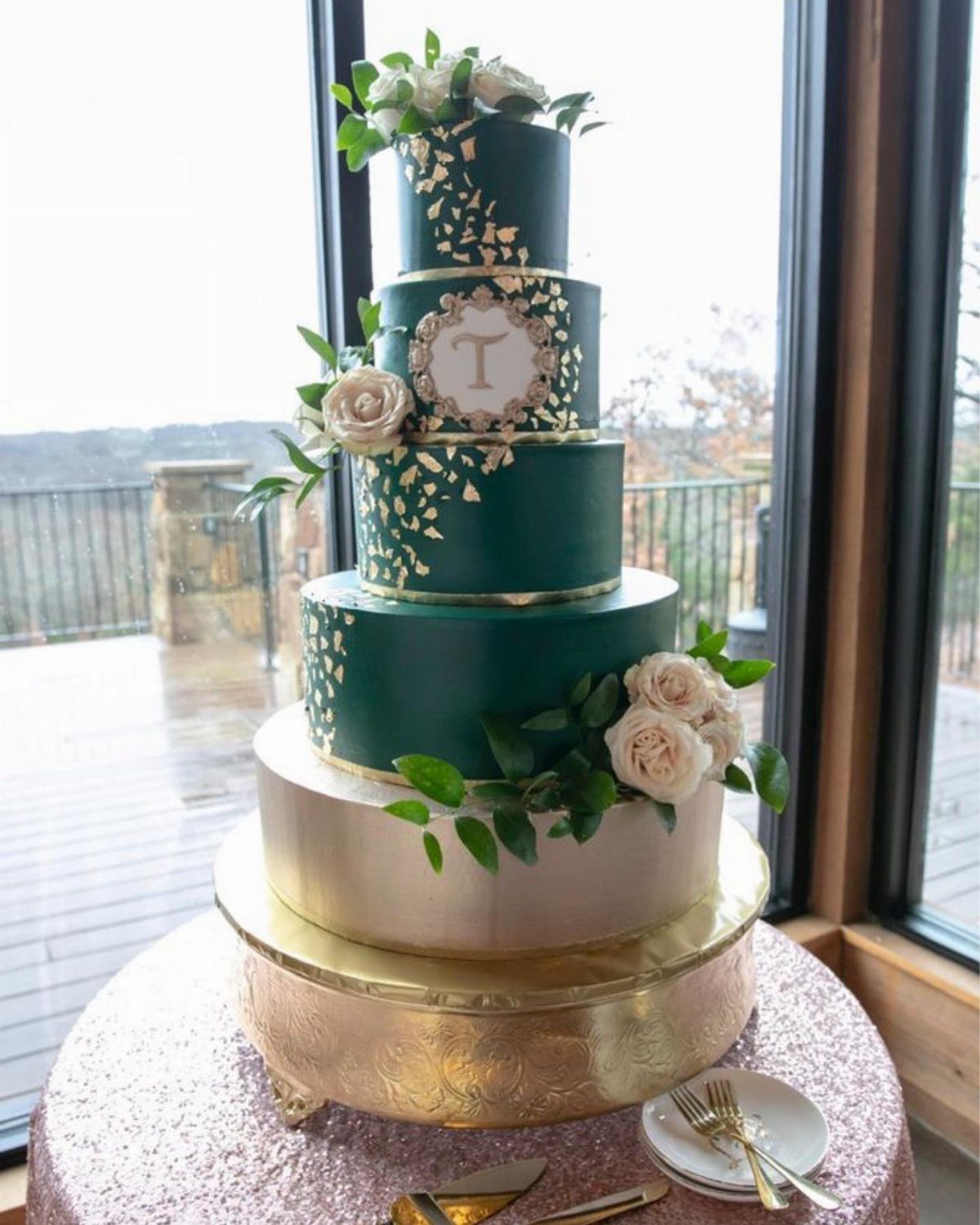 Five-tier emerald green and gold wedding cake decorated with white roses and foliage.