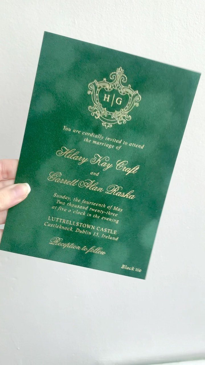 Emerald green wedding invitation with gold foil lettering held against a white background