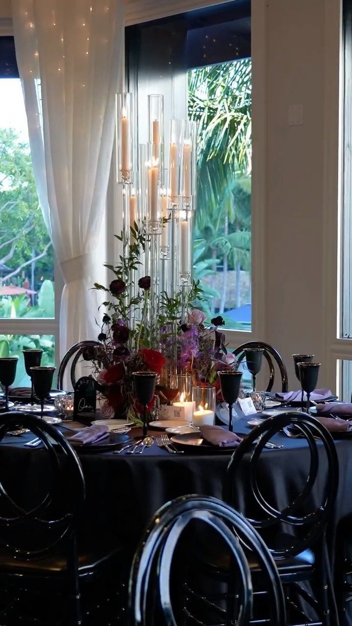 Wedding table setting with black linens, burgundy and purple floral centerpiece, and candles.
