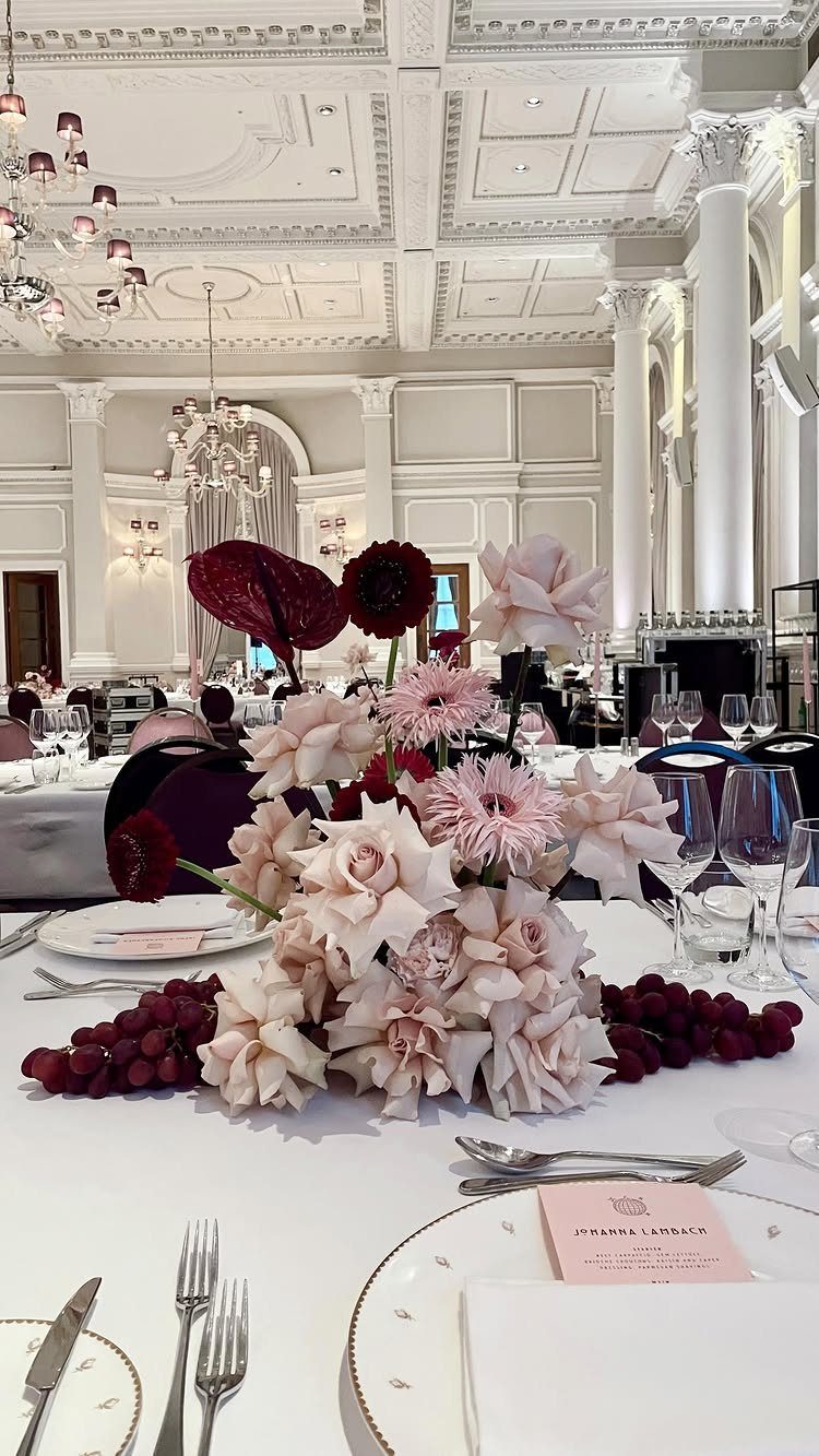 Floral centerpiece with burgundy and pale pink roses on a white wedding table.