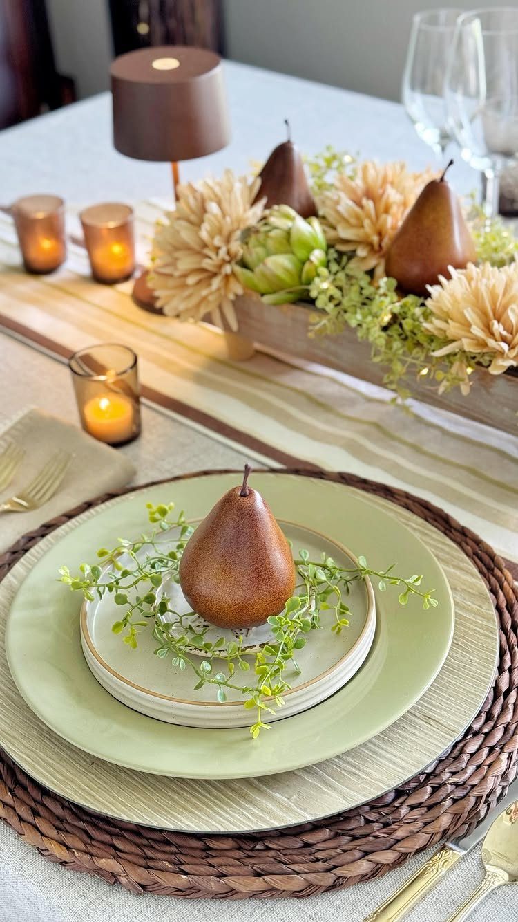 Table setting with green plates, brown pears, and beige floral centerpieces.