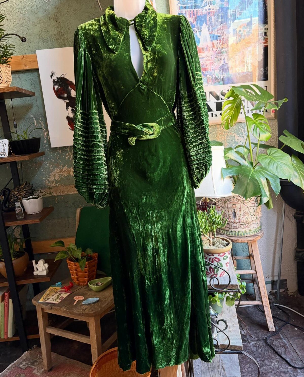 Emerald green velvet gown on a mannequin in a room with indoor plants.