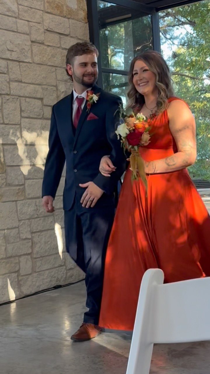 Couple in navy blue and burnt orange wedding attire with autumn floral bouquet.