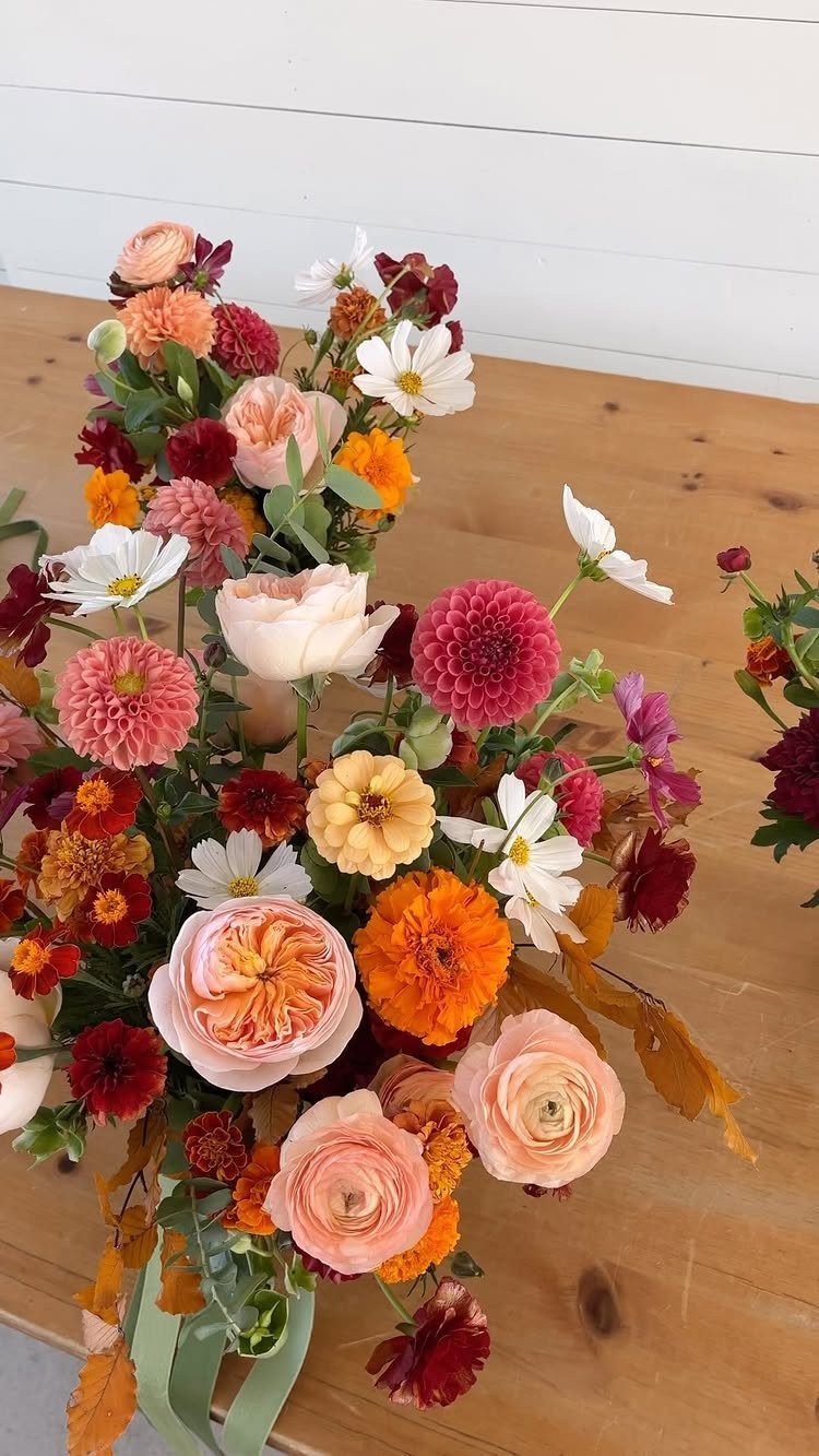 Floral bouquet with peach, orange, and burgundy blooms on a wooden table.