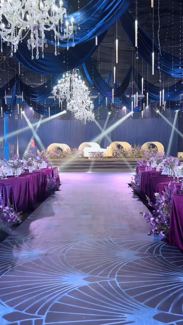 Navy blue ceiling drapes and purple banquet tables with floral arrangements in a ballroom