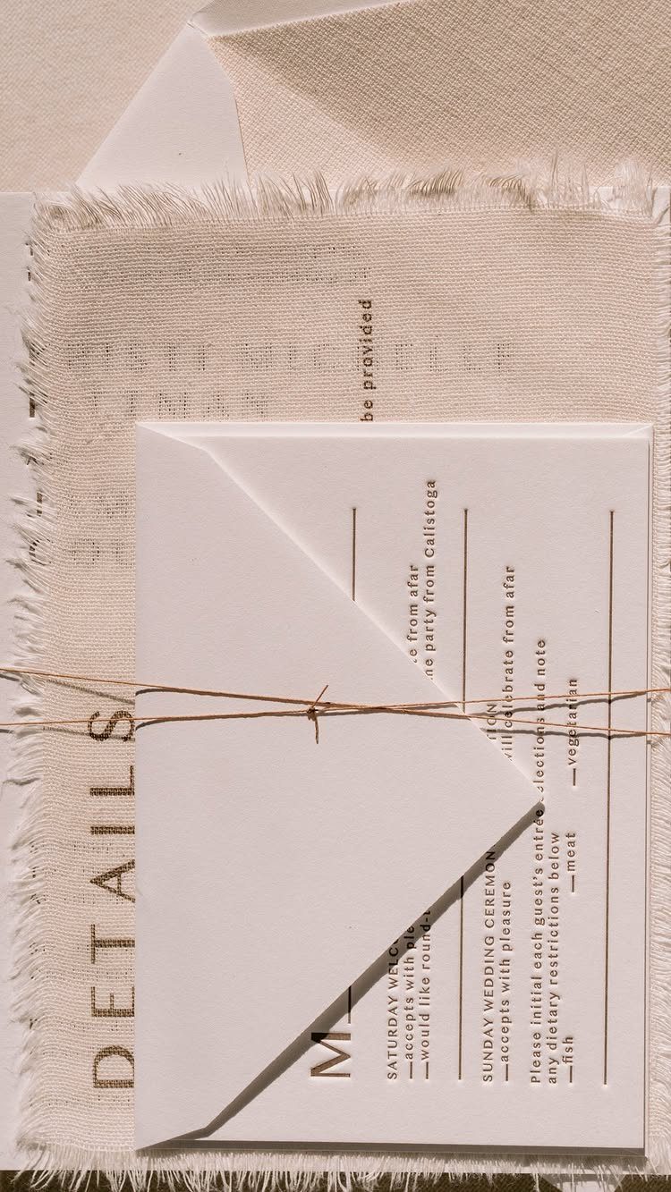 White wedding invitation tied with twine on a beige linen fabric background.