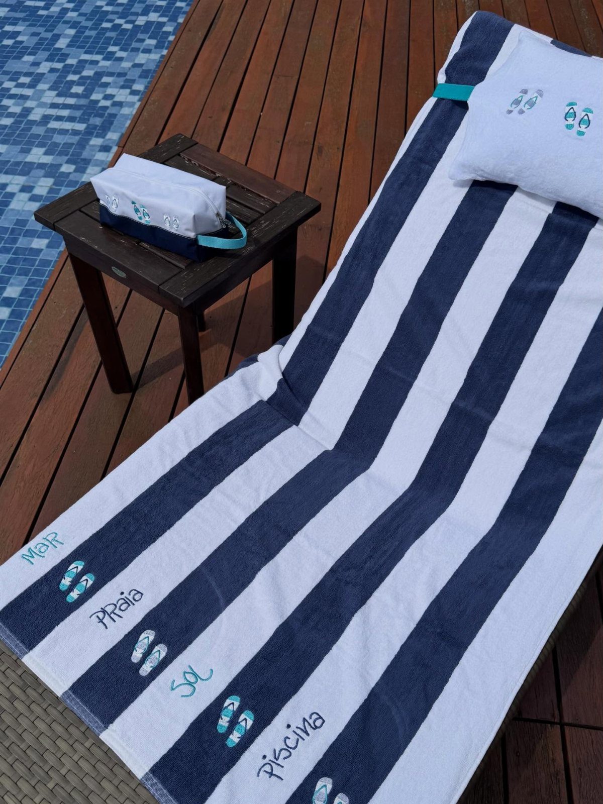 Blue and white striped beach towel with text on a wooden pool deck.