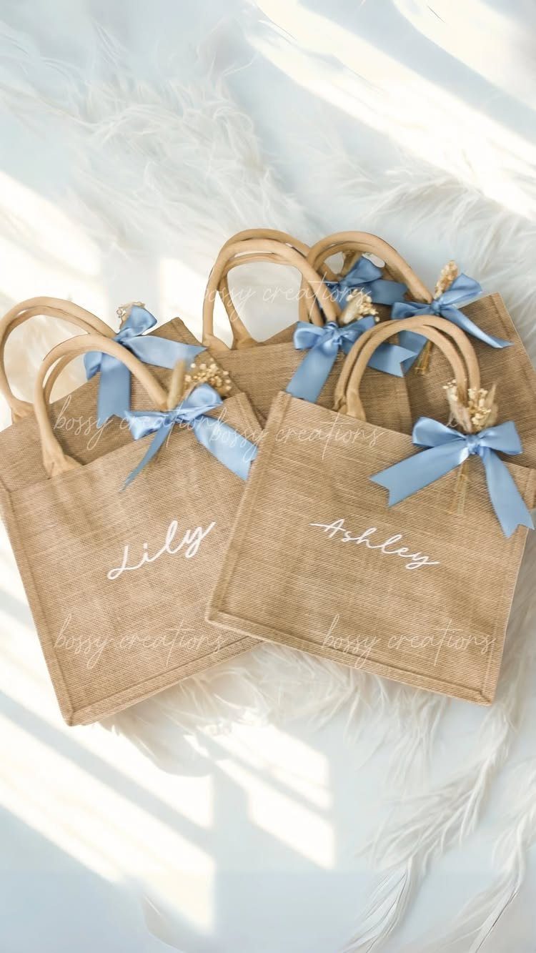Burlap tote bags with blue ribbons and personalized names on white fur.