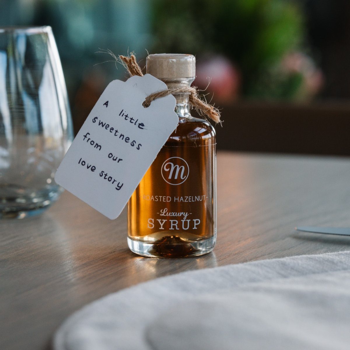 Small bottle of hazelnut syrup with a romantic wedding favor tag on wood.