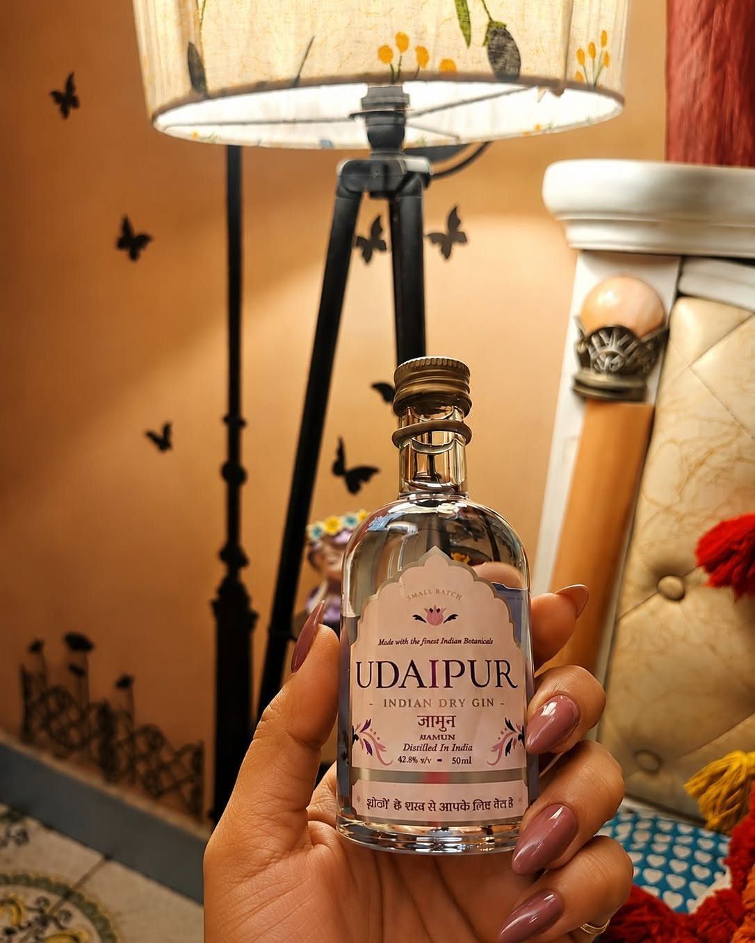 Small bottle of Udaipur Indian Dry Gin held by a hand with purple nails.
