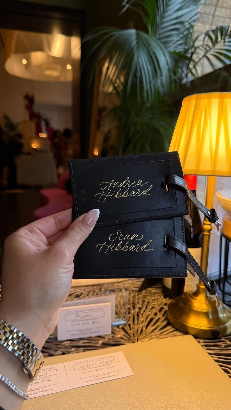 Black leather luggage tags with gold cursive names held by a hand.