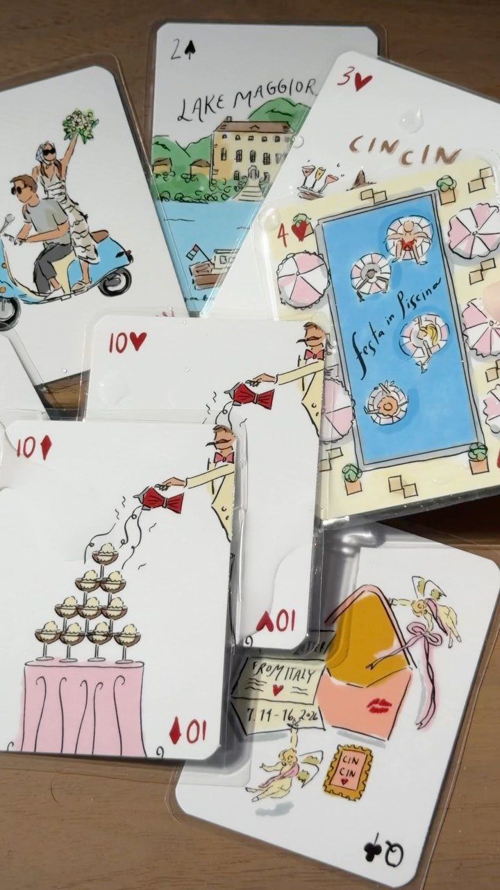Custom playing cards with colorful Italian-themed illustrations scattered on a wooden table.