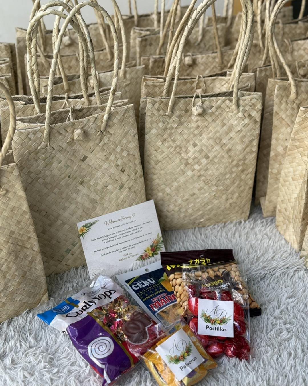 Woven straw bags and assorted packaged local sweets arranged with a welcome note.