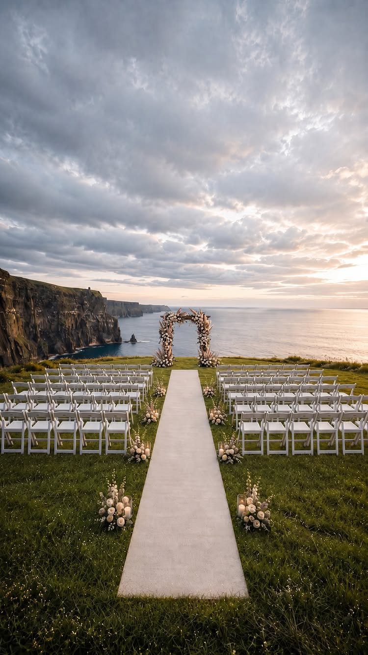 White wedding chairs and aisle runner leading to a floral arch on a cliffside.