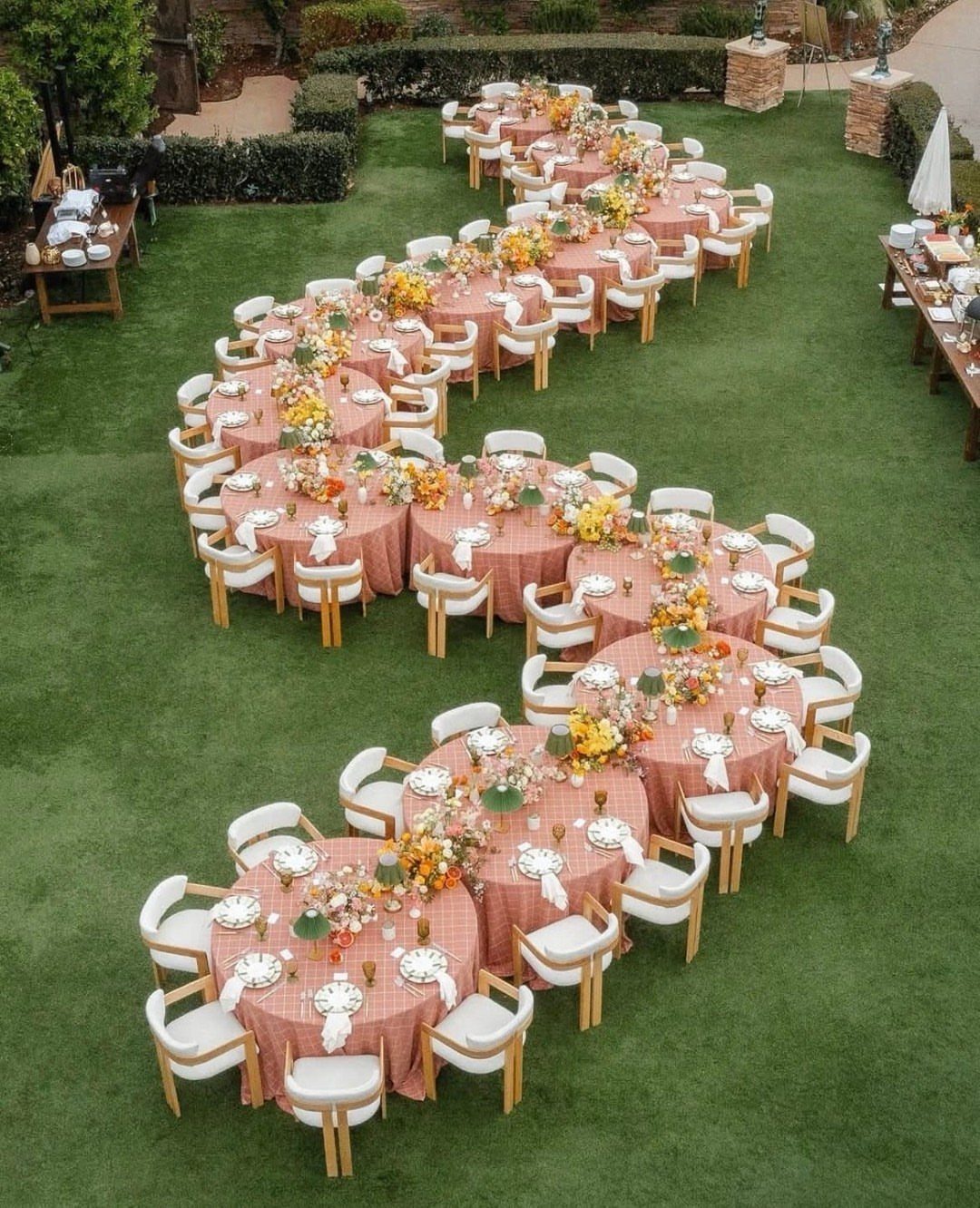Round dining tables with pink linens and white chairs arranged on green grass.