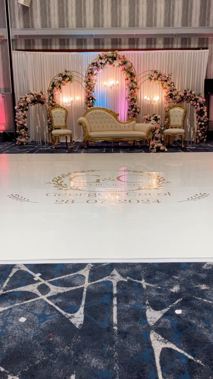 White glossy dance floor with gold monogram in front of a floral wedding stage.