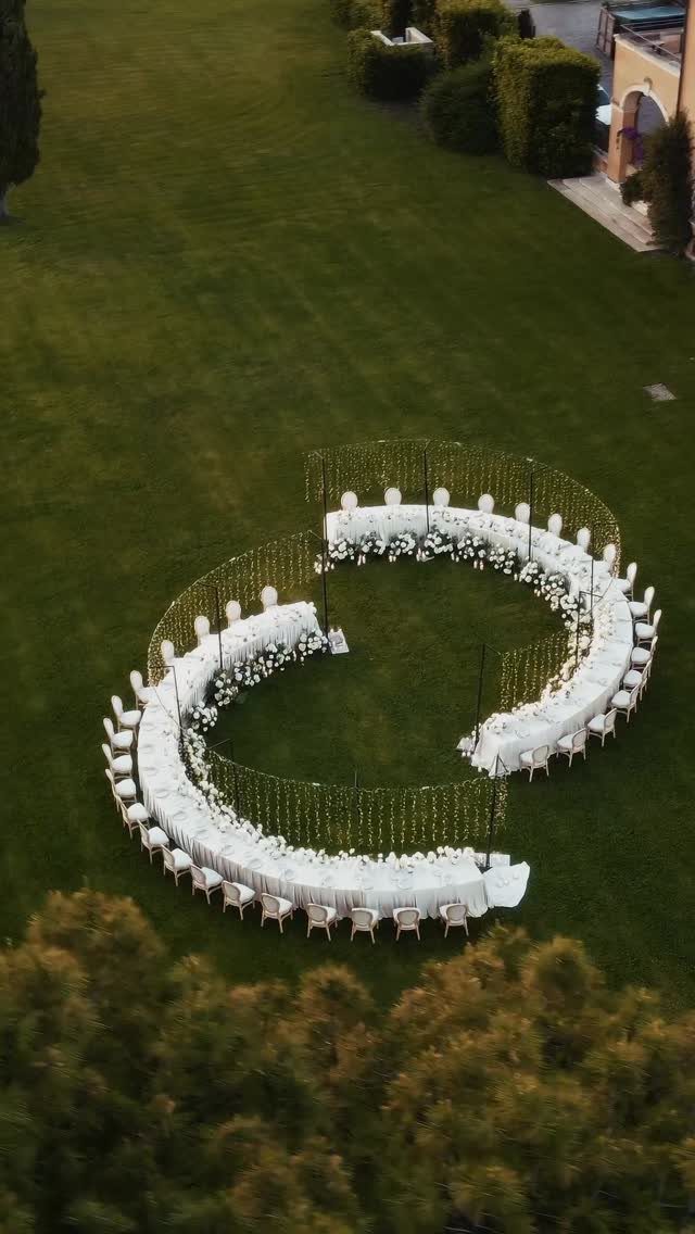 Curved white wedding head table with chairs on a green lawn outdoors.
