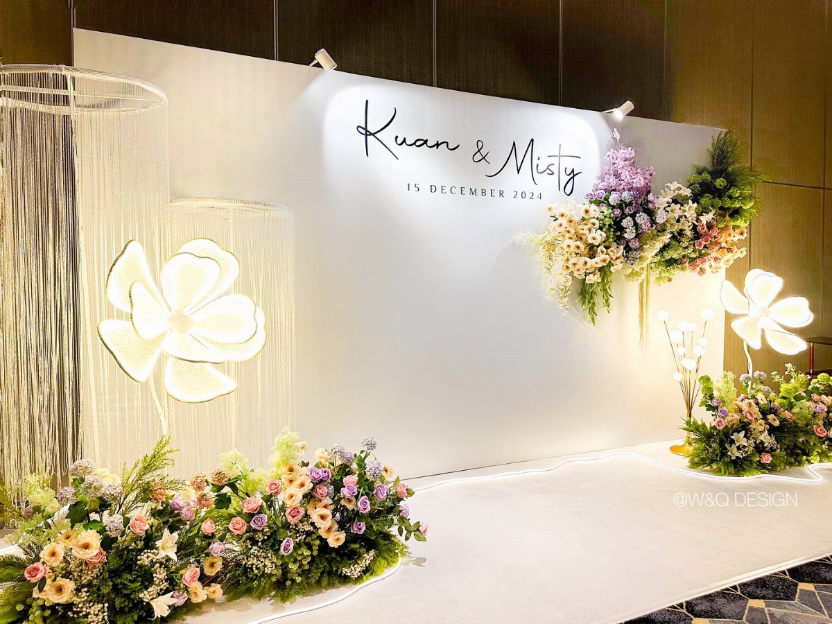 White wedding backdrop with colorful flowers, glowing flower lights, and metallic fringe curtains.