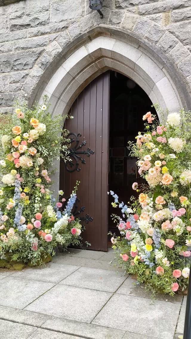 Pastel floral arrangements framing a stone arched doorway with a brown wooden door.