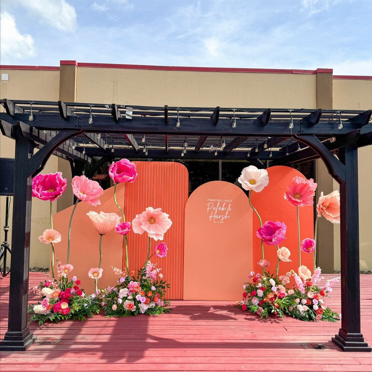 Oversized pink and orange poppy flowers arranged before orange arched backdrop panels.