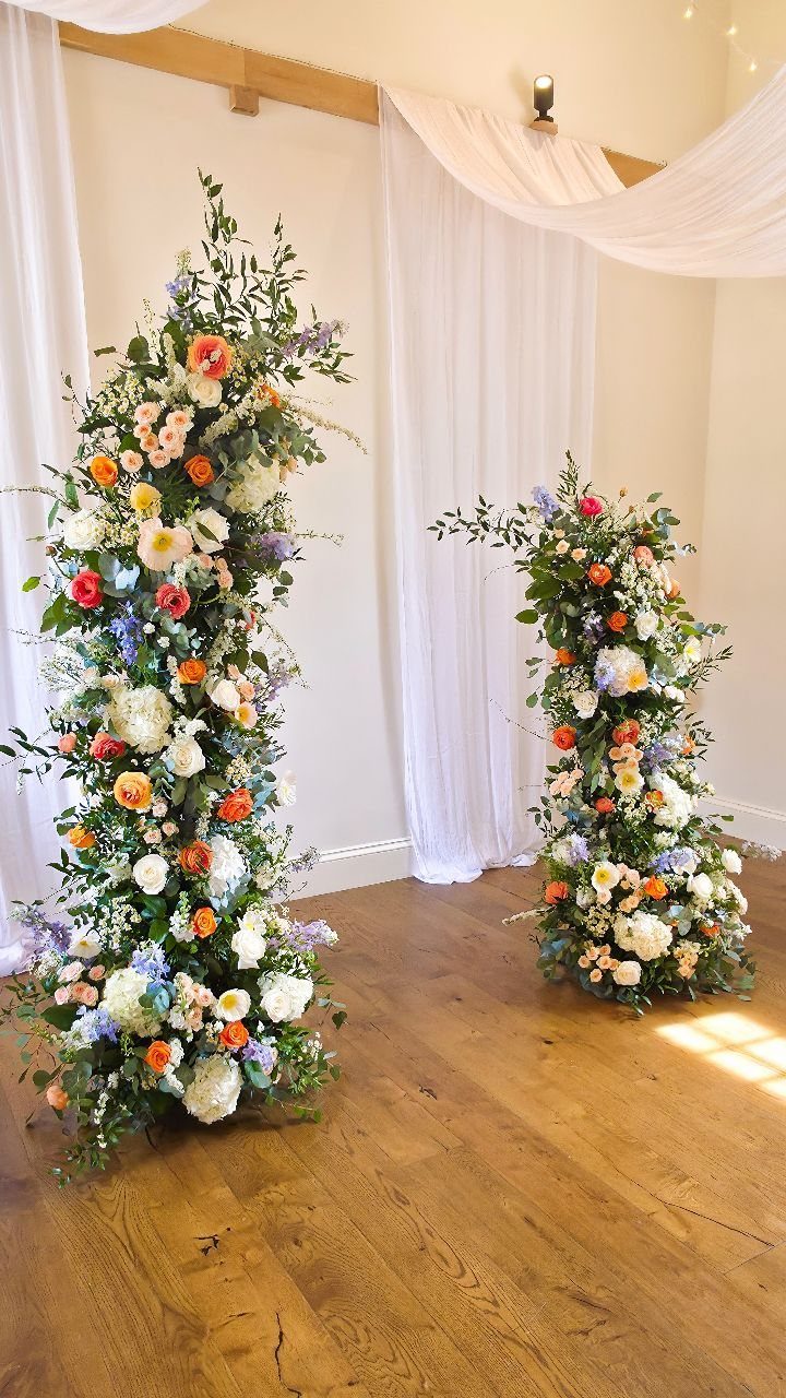 Two vertical floral pillars with colorful blooms and greenery on a wooden floor.