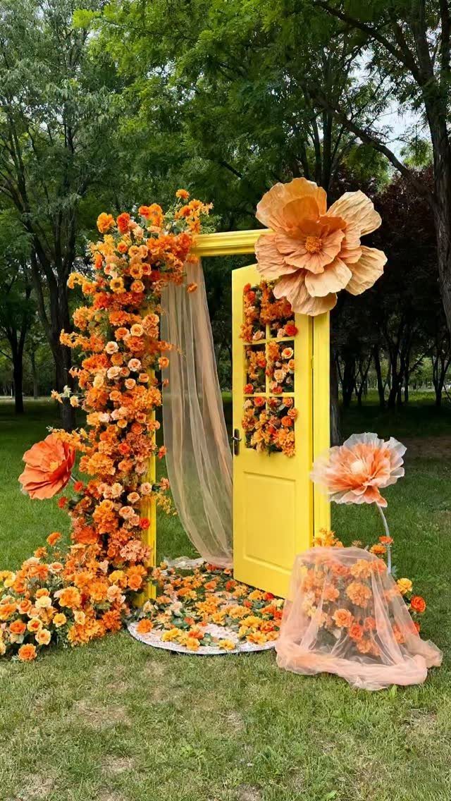Yellow door frame decorated with orange flowers and oversized paper floral accents outdoors.