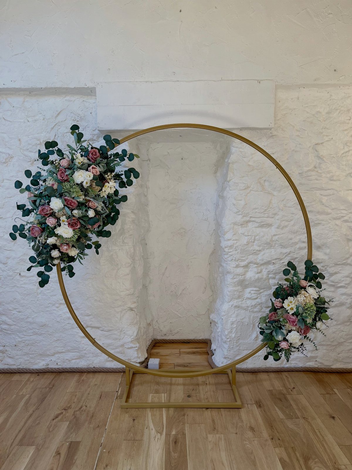 Gold circular moon gate arch decorated with pink and white floral arrangements.