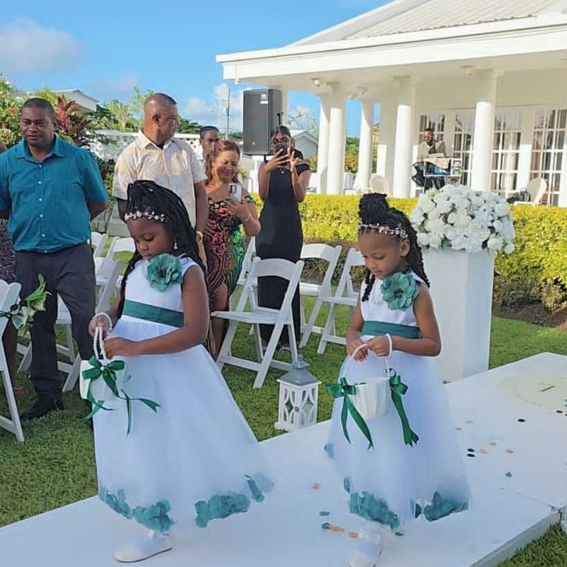 Two flower girls in white and teal dresses holding petal baskets on a wedding aisle